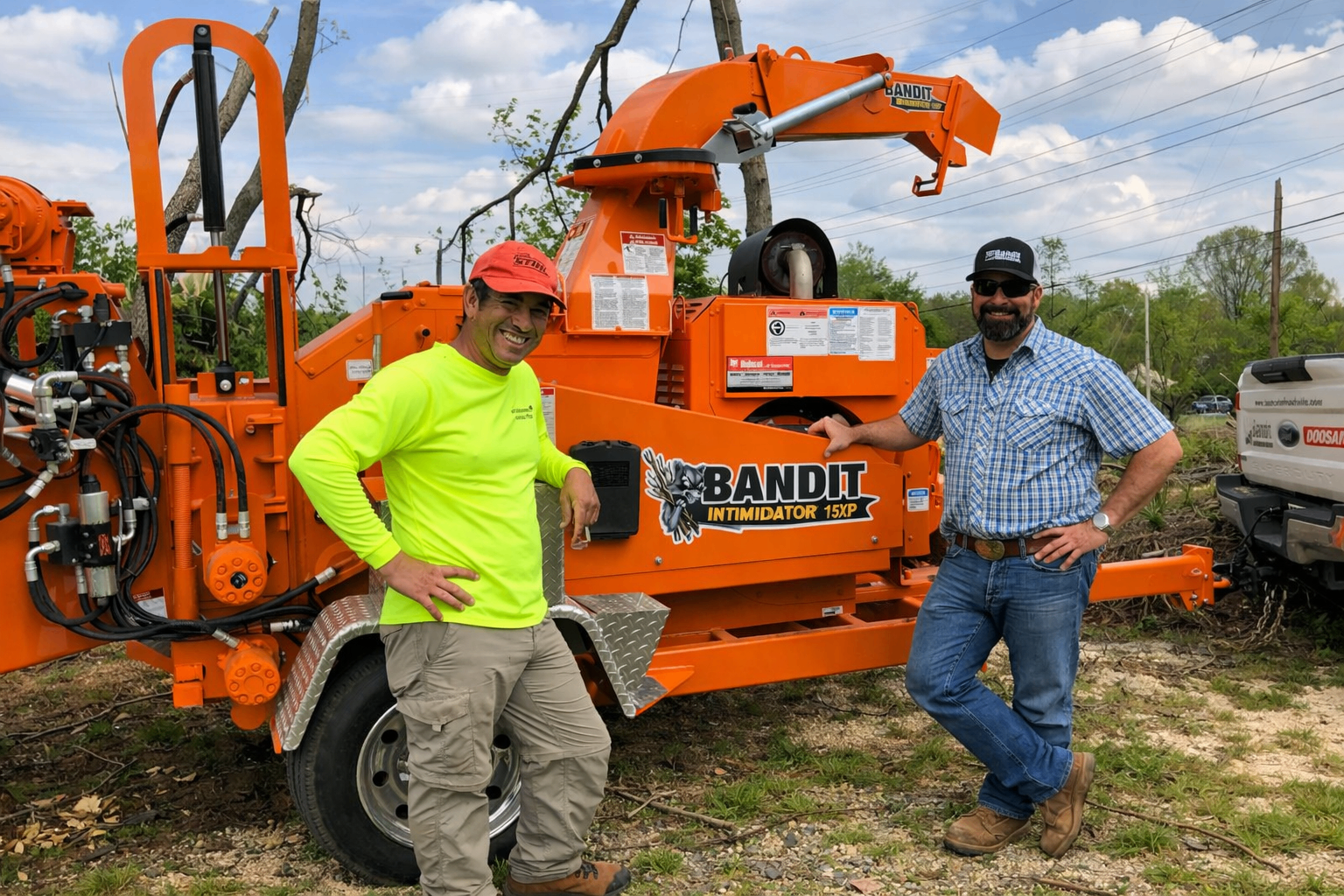 Two collaborators posing proudly beside an orange Bandit machine on site