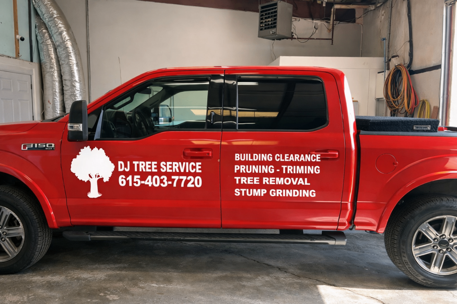 Red DJ Tree Service pickup truck with branding inside a garage